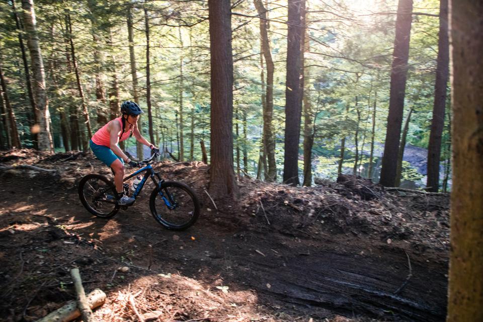 A woman rides a mountain bike down a dirt trail through the forest.
