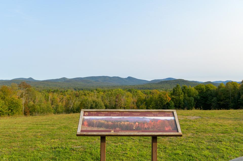 A scenic overlook with mountains in the distance and a sign identifying features in the foreground.