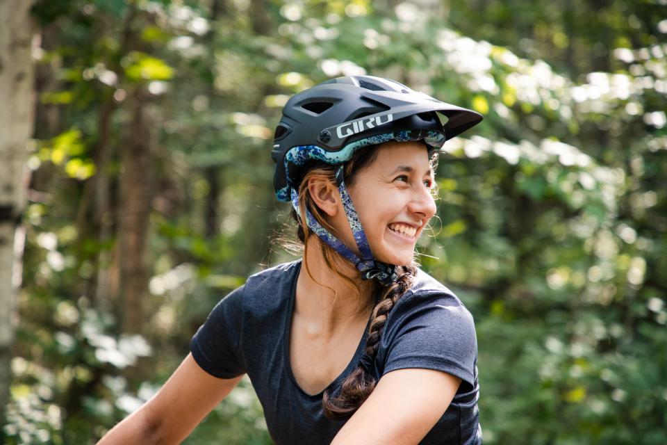 Close-up of a woman in a mountain bike helmet grinning in front of a leafy background.