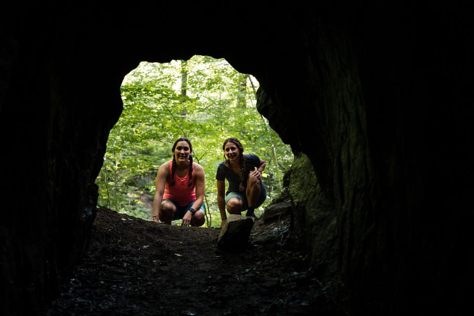 Two women peer into a cave, photo taken from inside the cave.