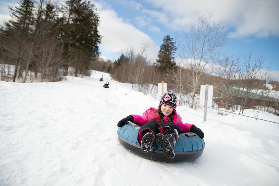 A child rides an inner tube down a snowy slope.