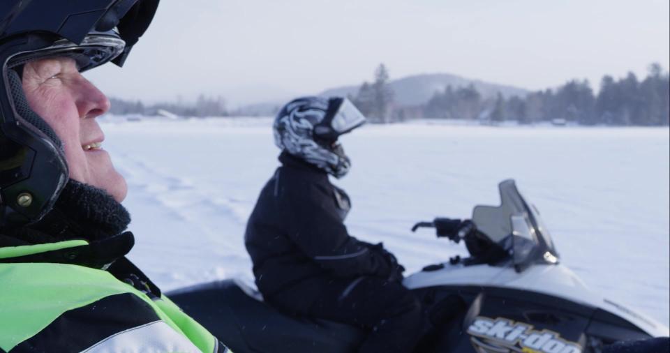 Two men stand beside their snowmobiles during a ride.