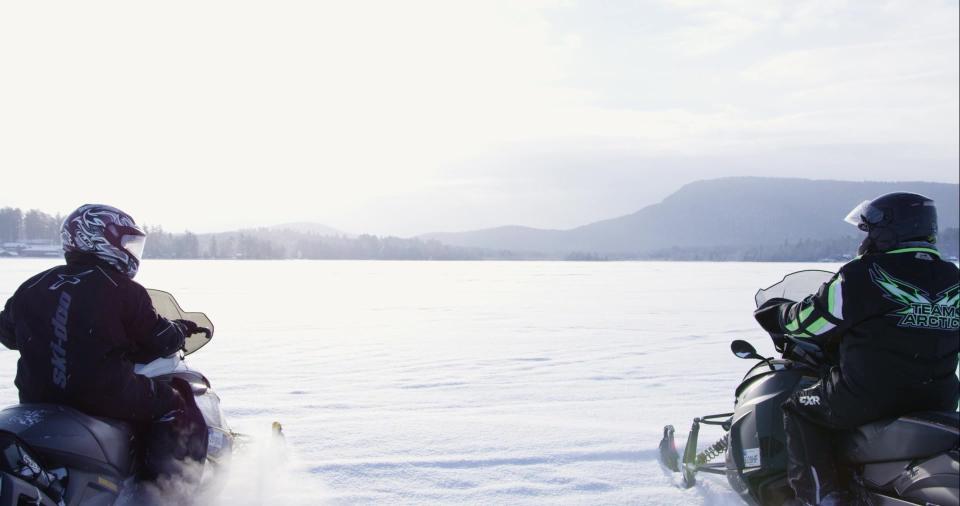 Two people sit on their snowmobiles on a frozen lake.