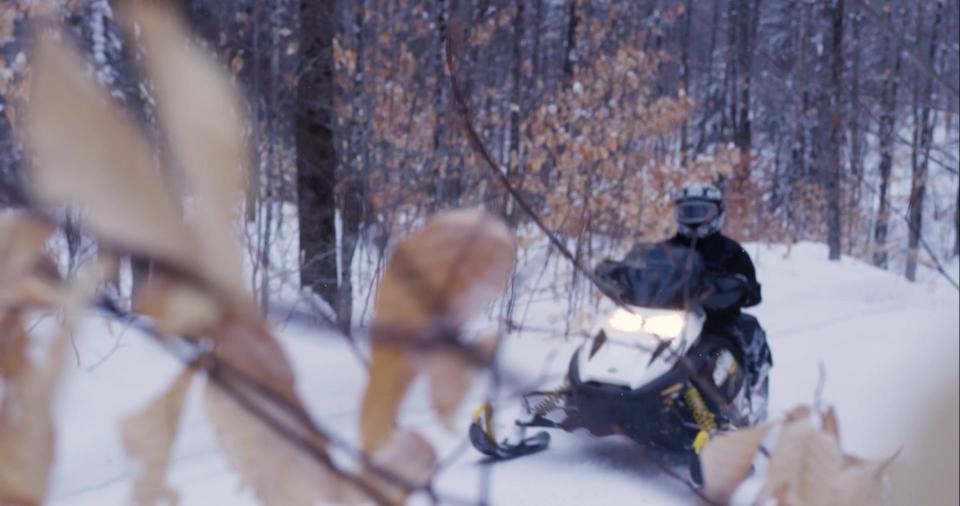 A person rides their snowmobile along a snowy trail through the woods