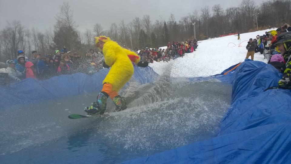 A man in a chicken costume on a snowboard participates in pondskimming to see how far he can get across the water.
