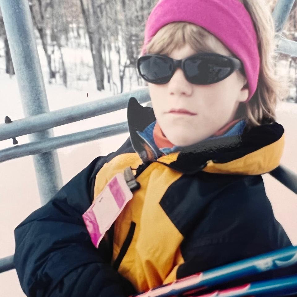 A child from the 90s in a yellow jacket, pink headband, and sick sunglasses blankly stares at the camera.