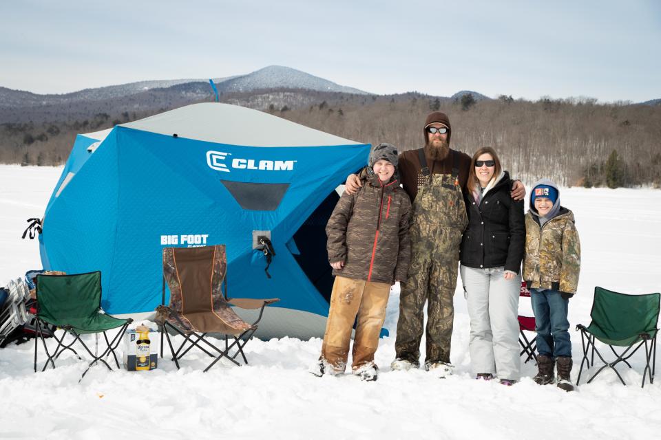 A family on the ice with an ice fishing shanty and chairs in the background.