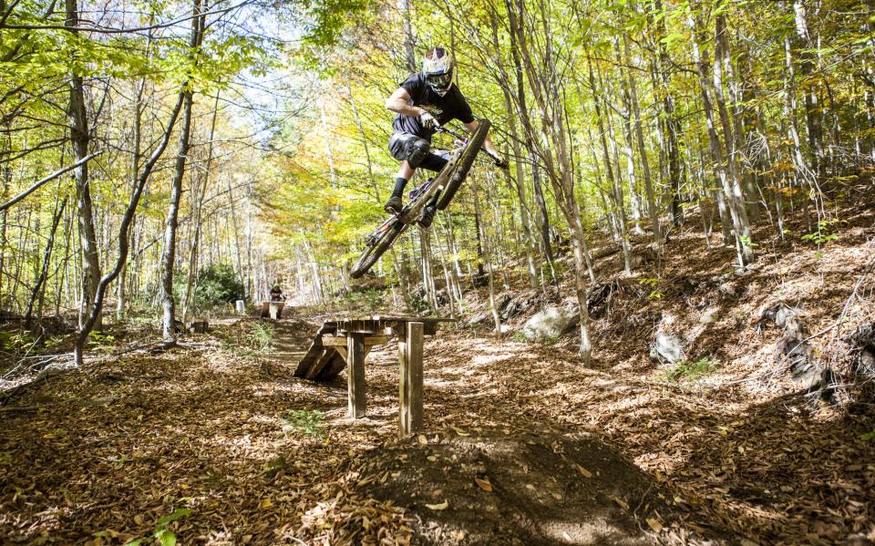 A mountain biker jumps off ramp on a wooded trail.