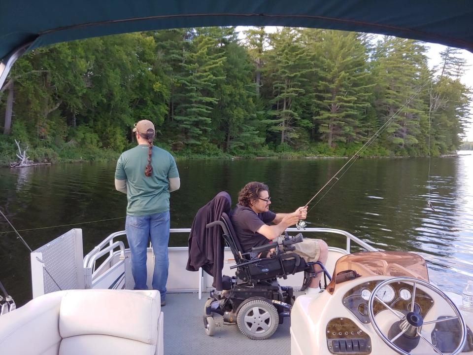 A man in a wheelchair and an individual standing fish from a wheelchair-accessible pontoon boat.