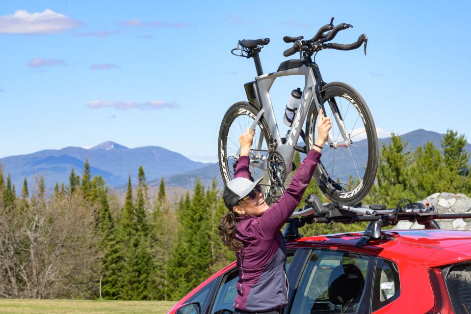 A woman takes her bike off of the roof rack of her car with mountains in the background.