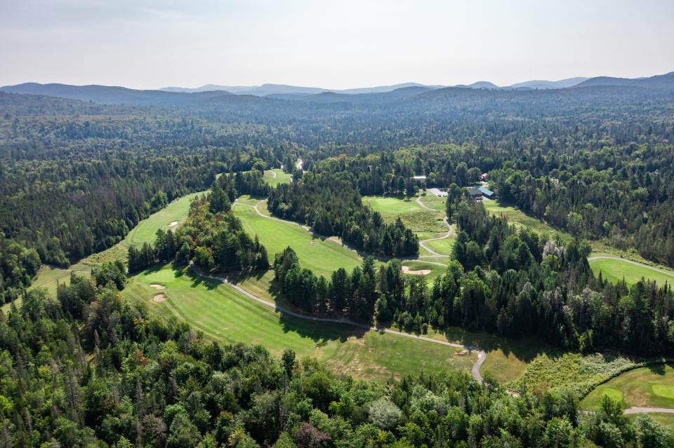 Aerial view of a golf course surrounded by forest and mountains.