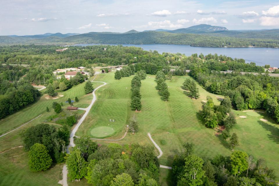 Aerial view of a golf course in the Adirondacks, with a large lake and mountains in the background.