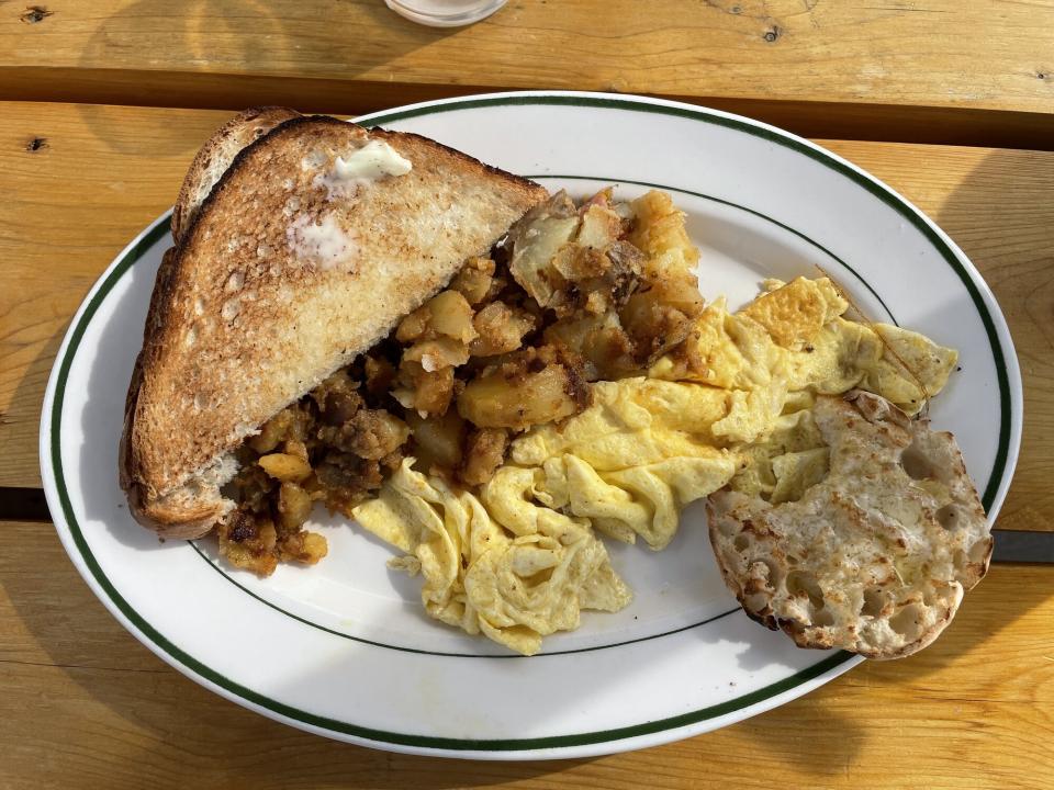 A plate of toast, potatoes, scrambled eggs, and an english muffin.
