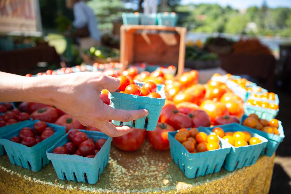 A hand reaches to grab a container of tomatoes on a stand