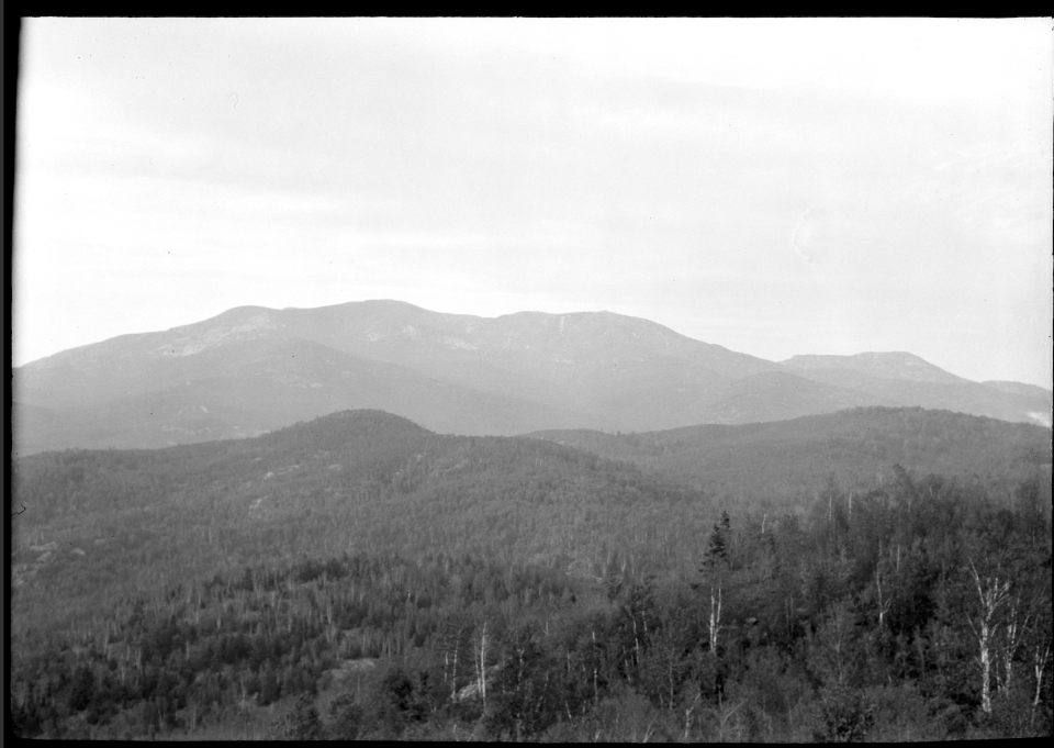 A black and white image of a distant mountain view from a mountain summit.