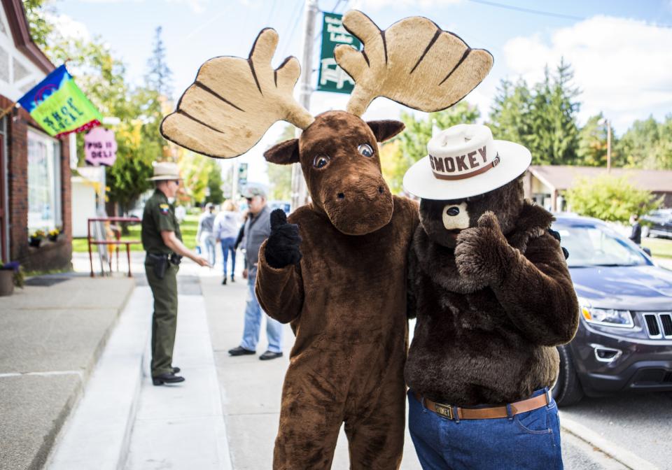 A human in a moose costume and a Smokey Bear give a thumbs up on the street