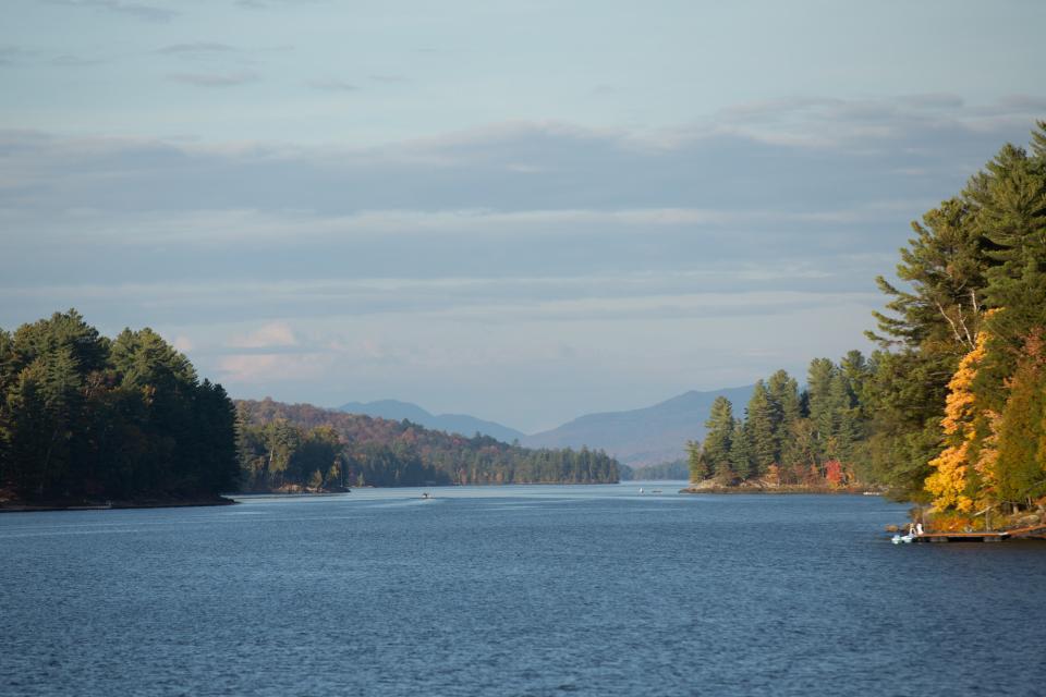 Looking straight down a narrow lake, with fall foliage and forests on either side.