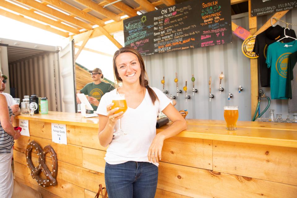 A woman holds a glass of cold beer at a rustic wooden bar.
