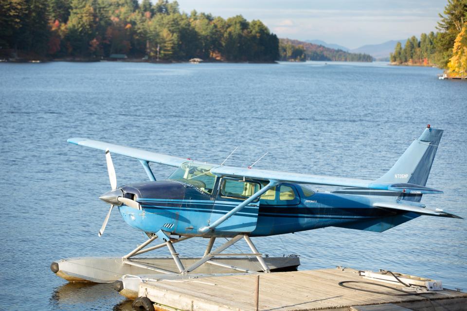 A blue floatplane on a lake with fall foliage.