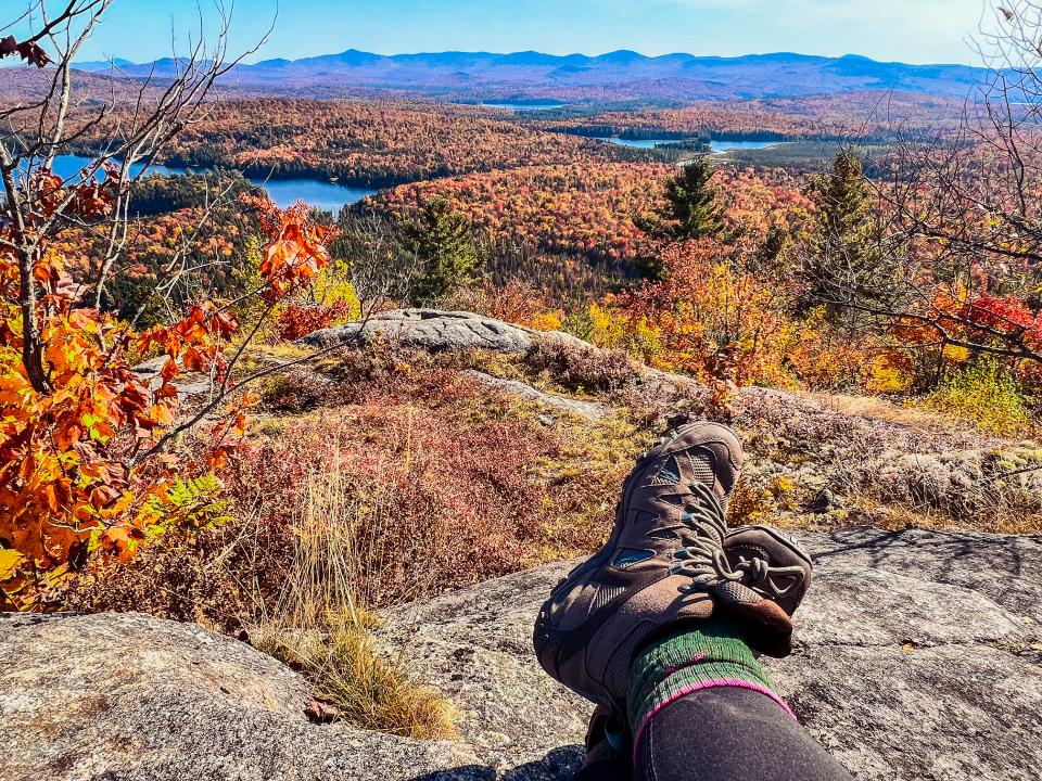 A hiker relaxes on the summit with legs crossed and fall views stretched out below.