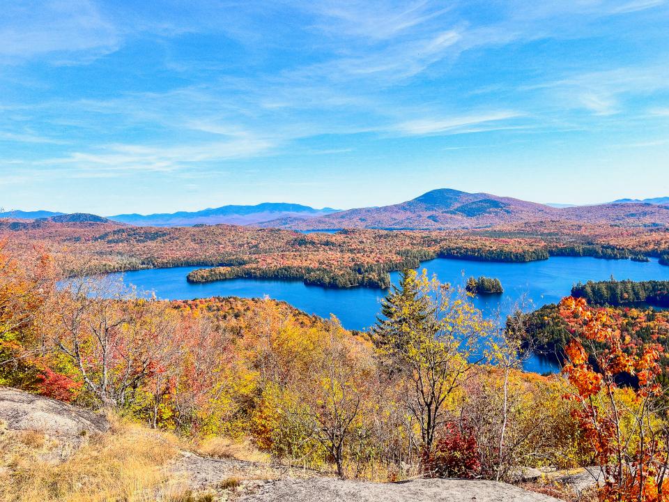 A panorama of a lake, mountains, and a bright fall forest with lots of peak foliage color.