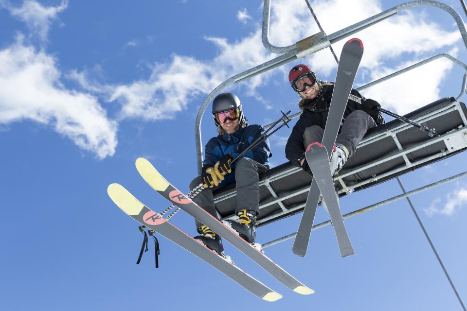 Two men with skis on look down from their chairlift.