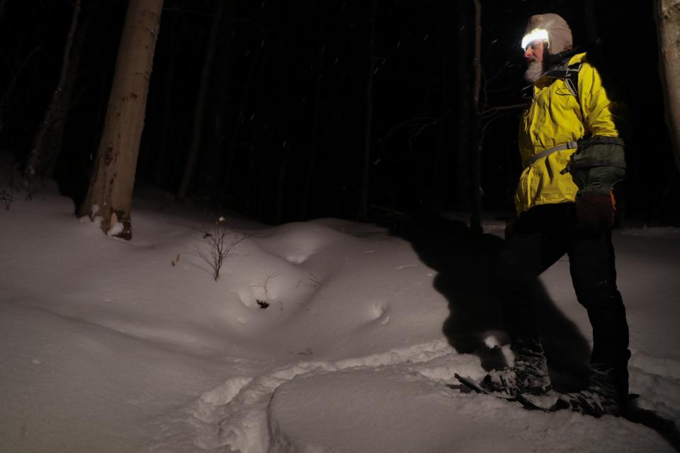 A hiker in the dark uses a headlamp to light the trail in front of him