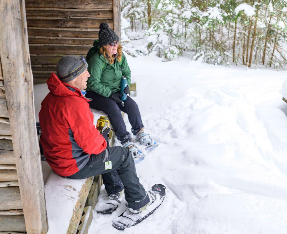 A couple takes a break from snowshoeing in a lean-to with water to drink