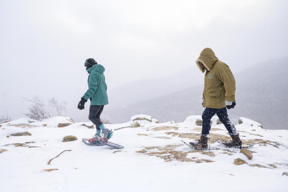 Two snowshoes walk through blizzard conditions on a mountain summit