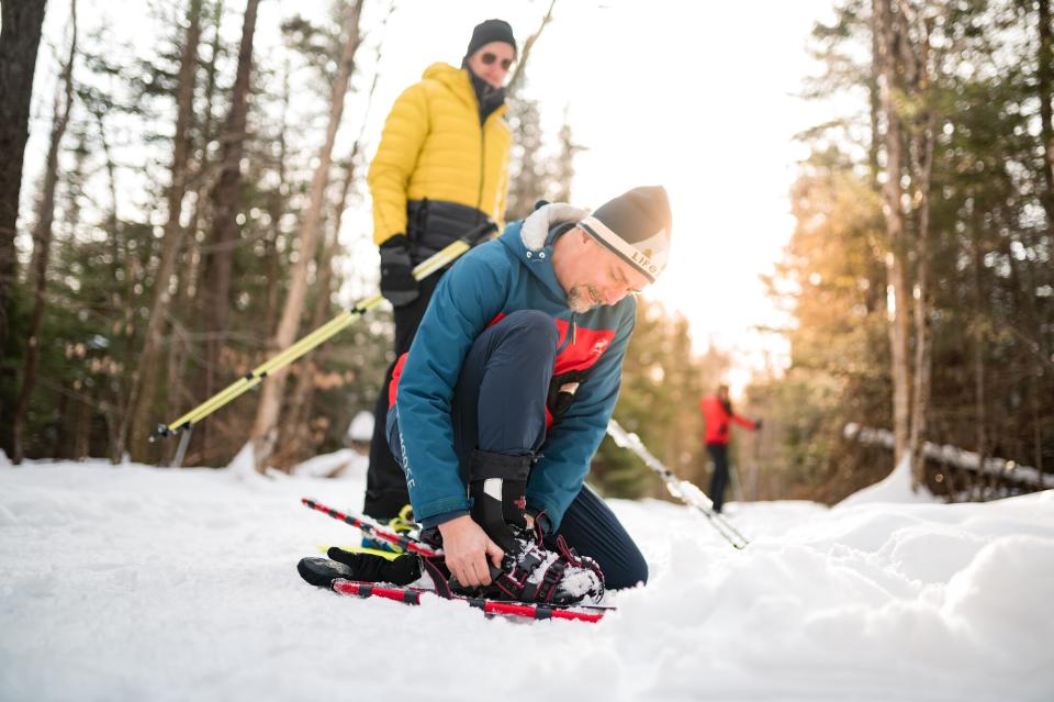 A man straps his snowshoes on his feet on a snowy trail