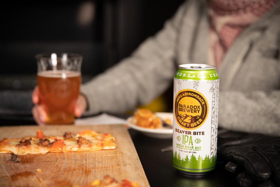 a man sips on a drink next to a slice of pizza and a paradox brewery IPA.