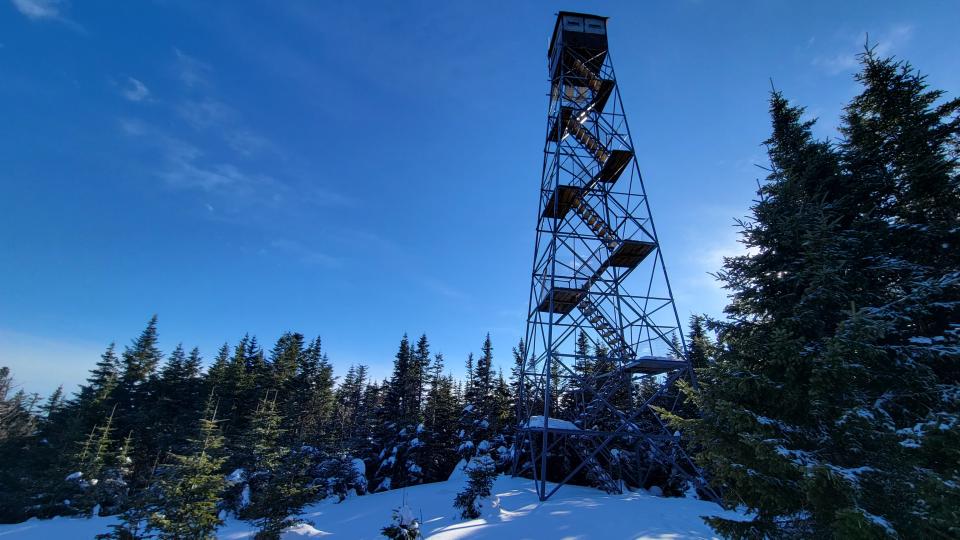 Pillsbury Firetower soars above a snowy summit crowded with evergreen trees.