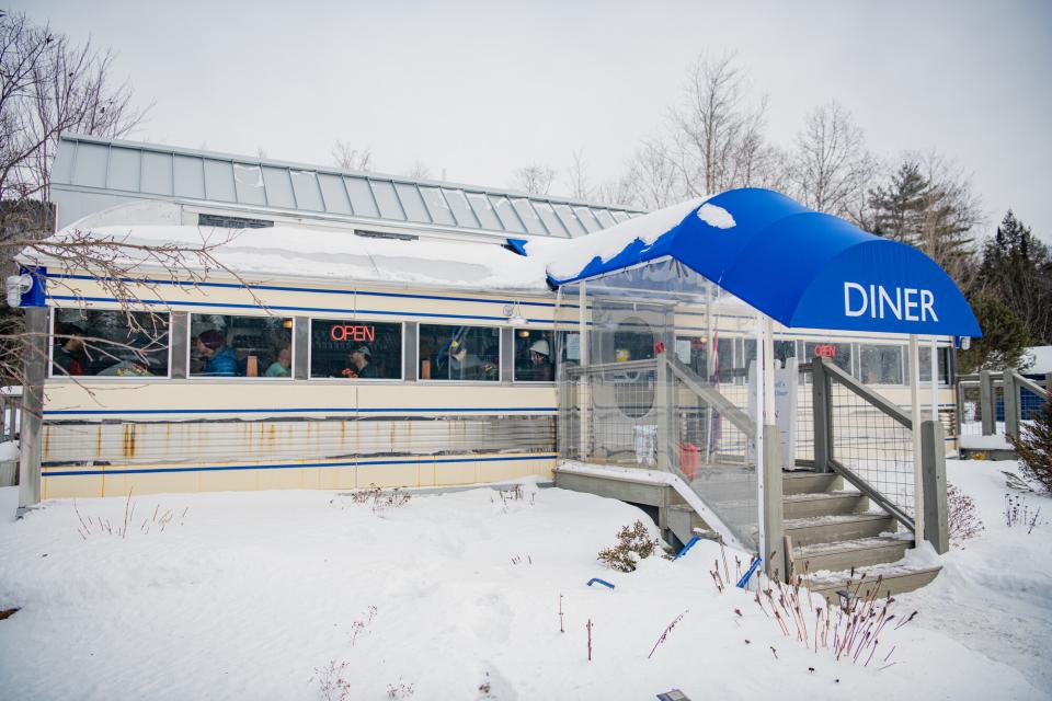 A vintage diner with silver siding and a blue awning in the snow.