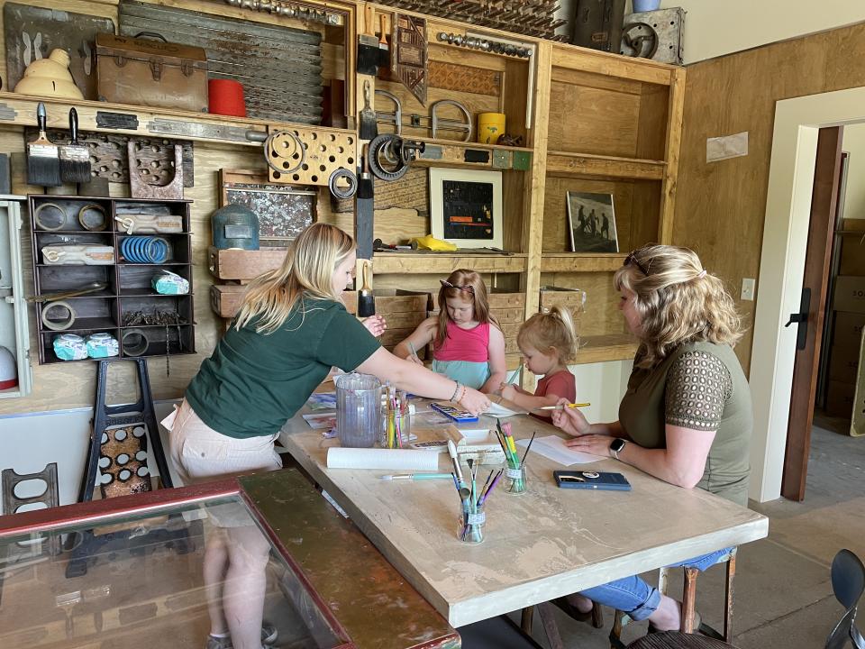 Two kids and two adults work on an art project on a wooden work bench
