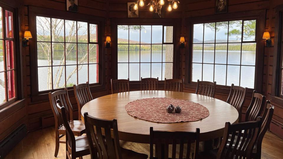 A curved dining nook is filled with windows overlooking a blue lake. A round table sits in front of the windows.