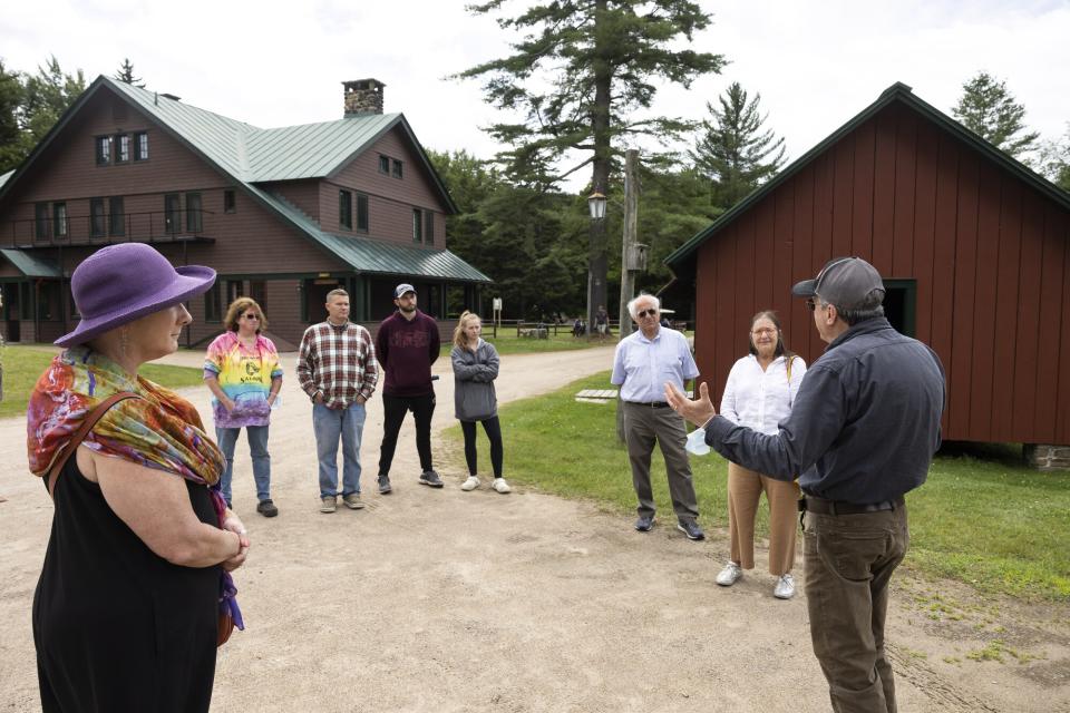 A group of people stand in a semi-circle on a history tour at an Adirondack Great Camp.