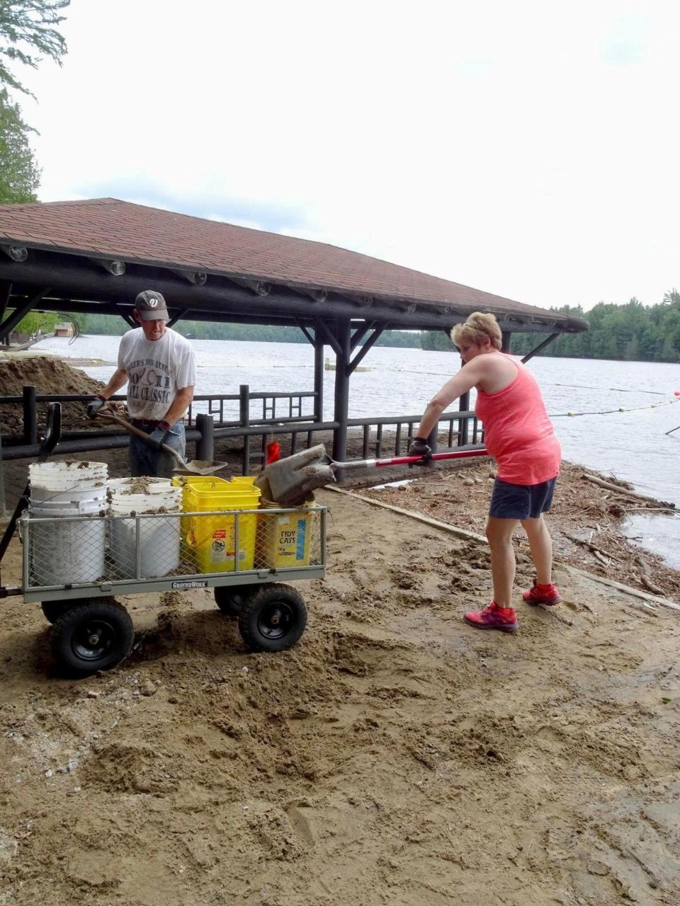 A man and woman clear debris from a boathouse on the water.