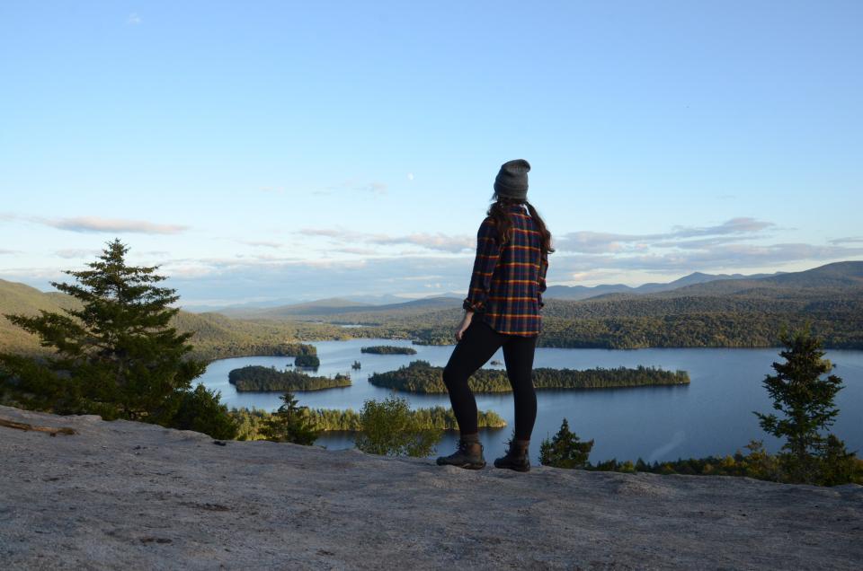 A woman stands on top of a mountain with lakes below.