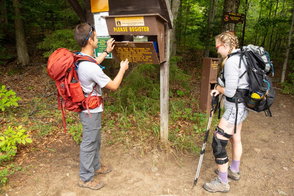 A man and woman sign into a trail with gear on for a hike.