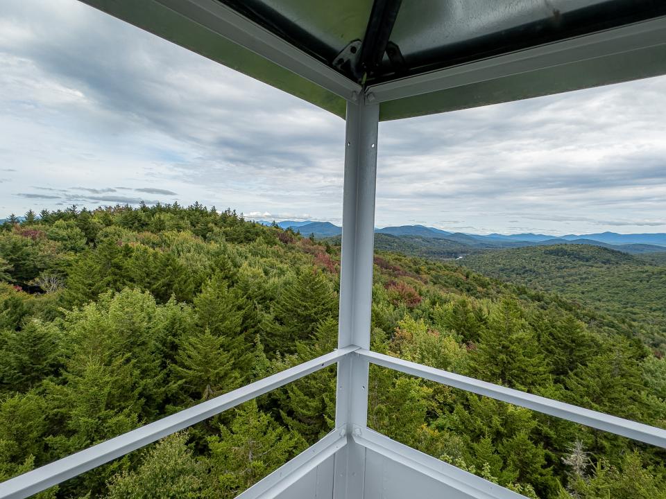 A forested view from a fire tower cabin with metal across the windows