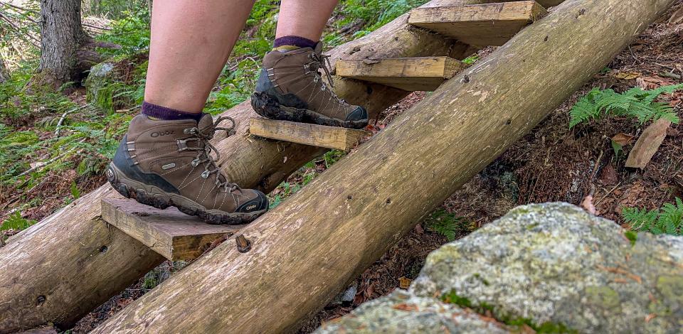 A hiker in brown hiking boots climbs a new wooden staircase on a hiking trail