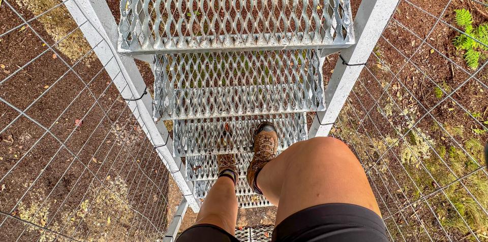 Someone hikes up the metal stairs of a fire tower wearing brown hiking boots.