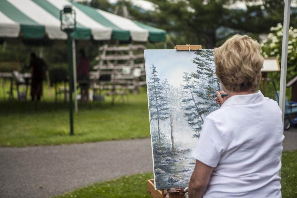 a woman paints a cold winter scene with evergreen trees on canvas.