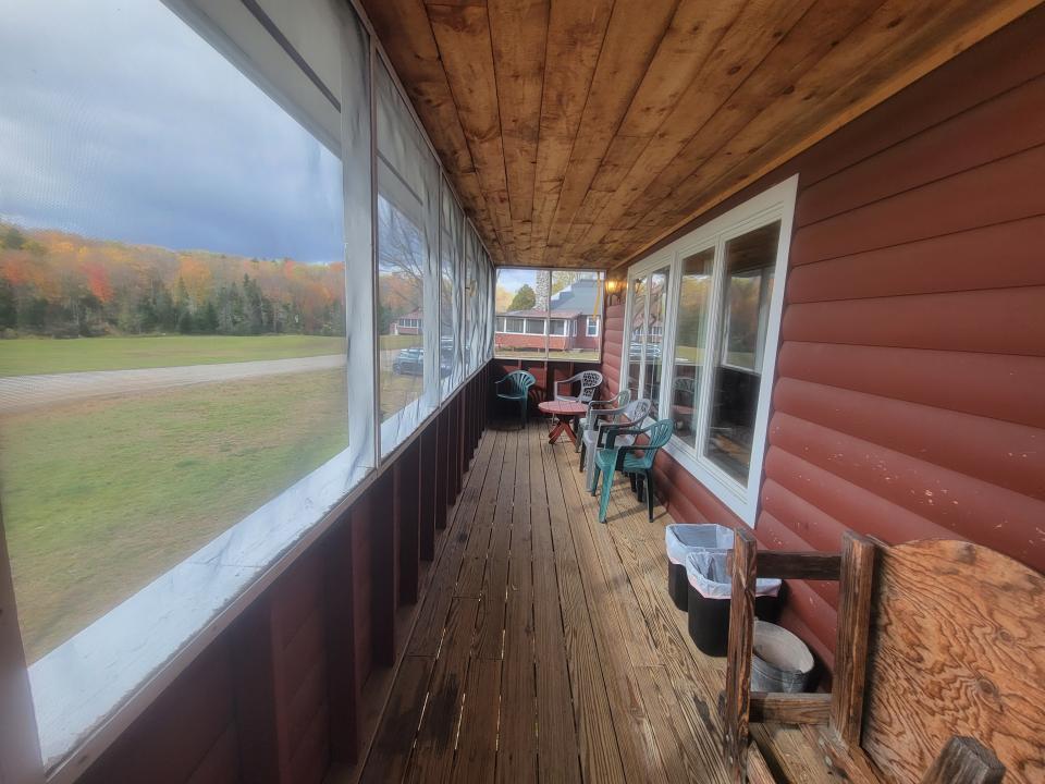 A large screened-in porch overlooks a flat field with fall foliage in the distance.