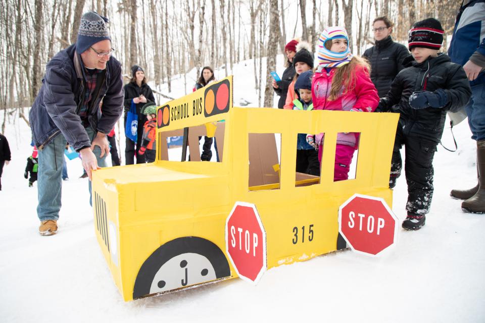 Adults and kids participate in a card board sled race with a sled decorated like a school bus