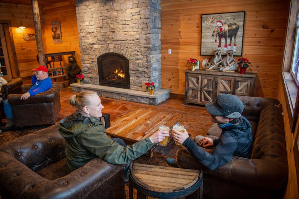 A couple toast glasses of beer near a fireplace indoors at The Lemon Tree brewery in Speculator