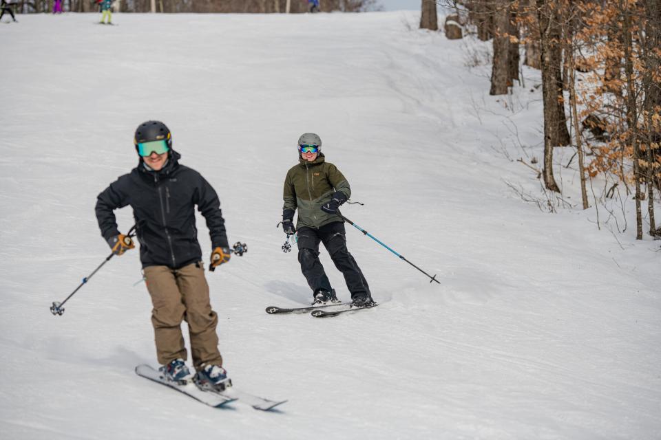 Two people ski down a downhill slope at Oak Mountain Ski Center