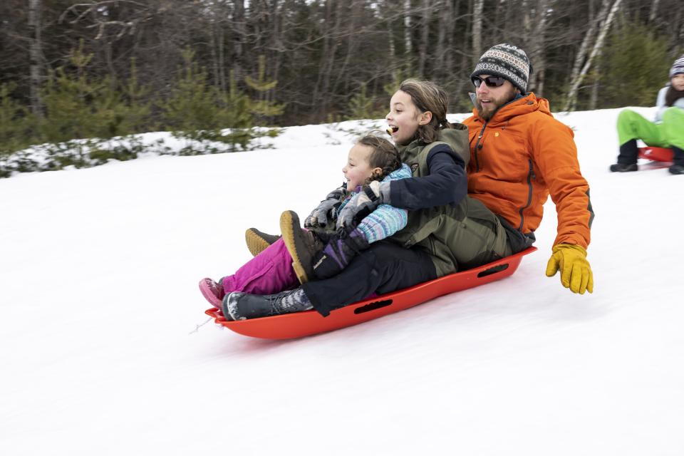 A man and two children crowd onto a sled on a snowy slope