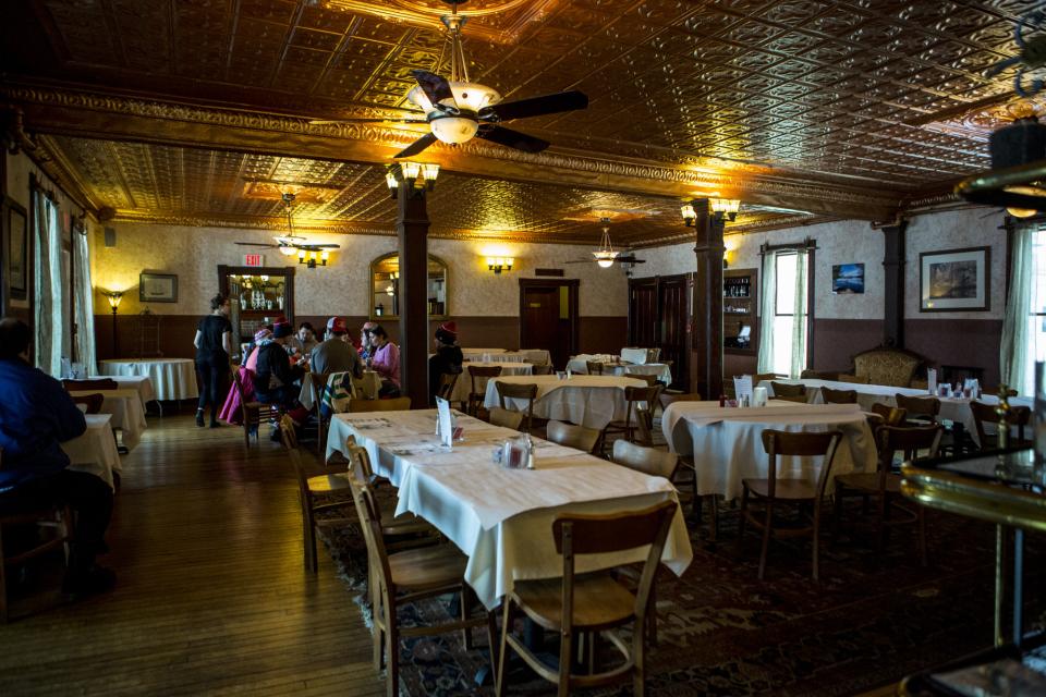 An inn dining room featuring pressed tin ceiling, antique lighting, and an array of tablecloth-covered tables.
