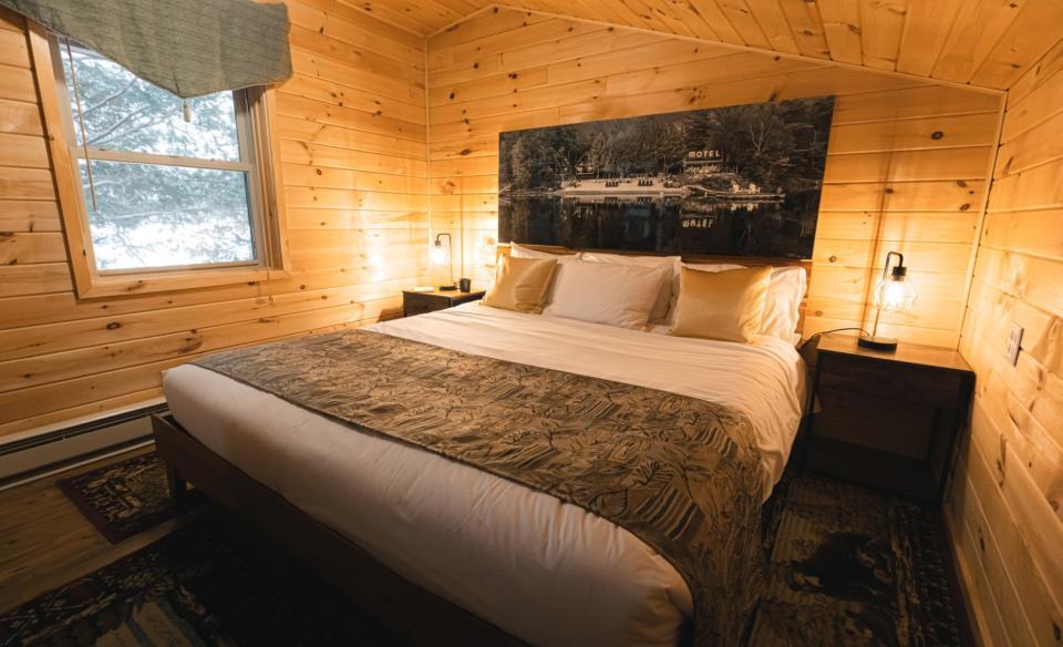 A rustic-modern Adirondack motel room featuring lightly-colored wood paneling, large bed, and cozy touches.